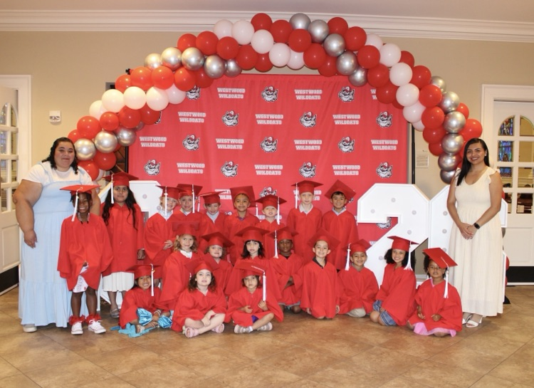 Mrs. Landeros’ and Ms. Sanchez’s class wearing their caps and gowns for graduation standing in front of the ballon arch and the Westwood backdrop 