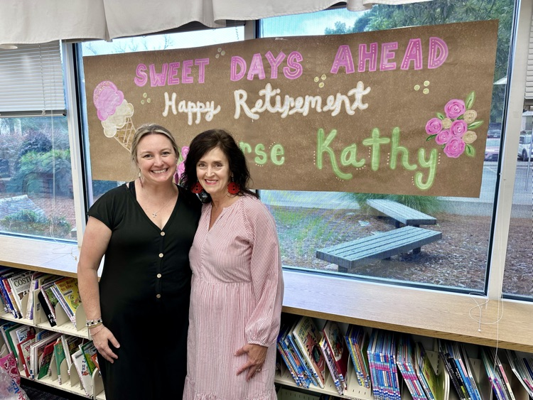 Nurse Kathy and Mrs Harrison standing in front of the sign that says “Sweet Days Ahead. Happy Retirement!