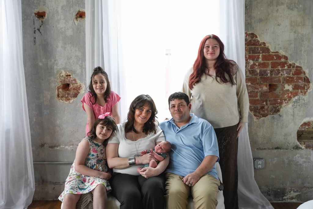 a family sits with a mother, father, 3 daughters, and a baby