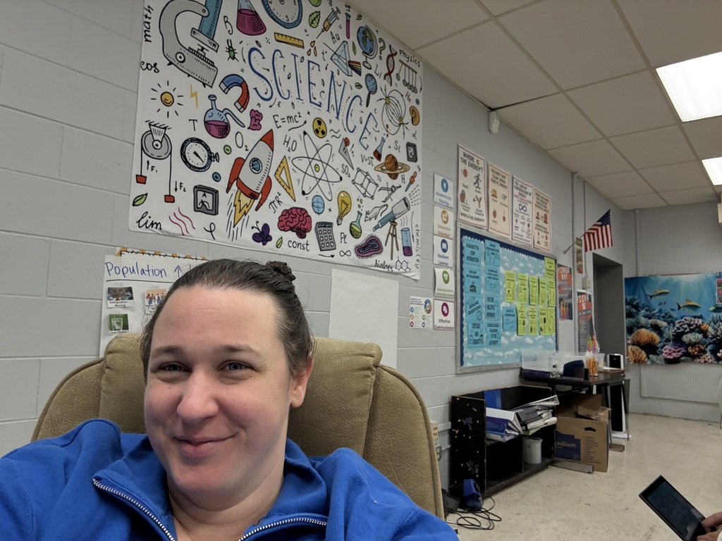 teacher sits at desk with poster begin her