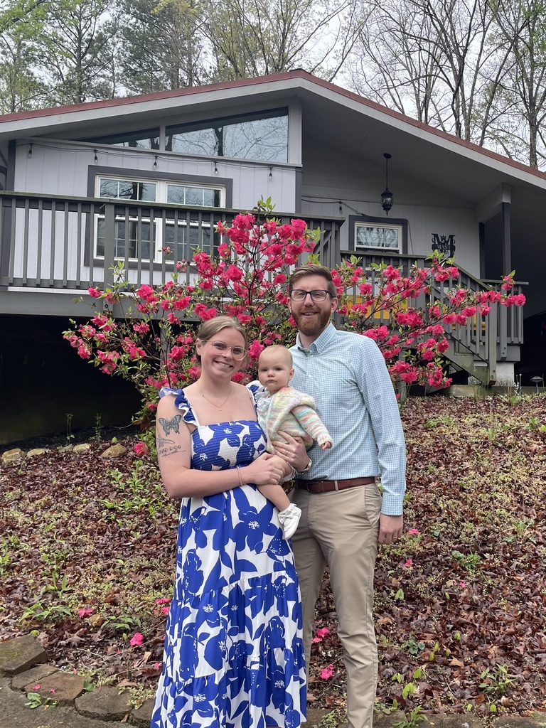 man, woman, and baby pose in front of a house