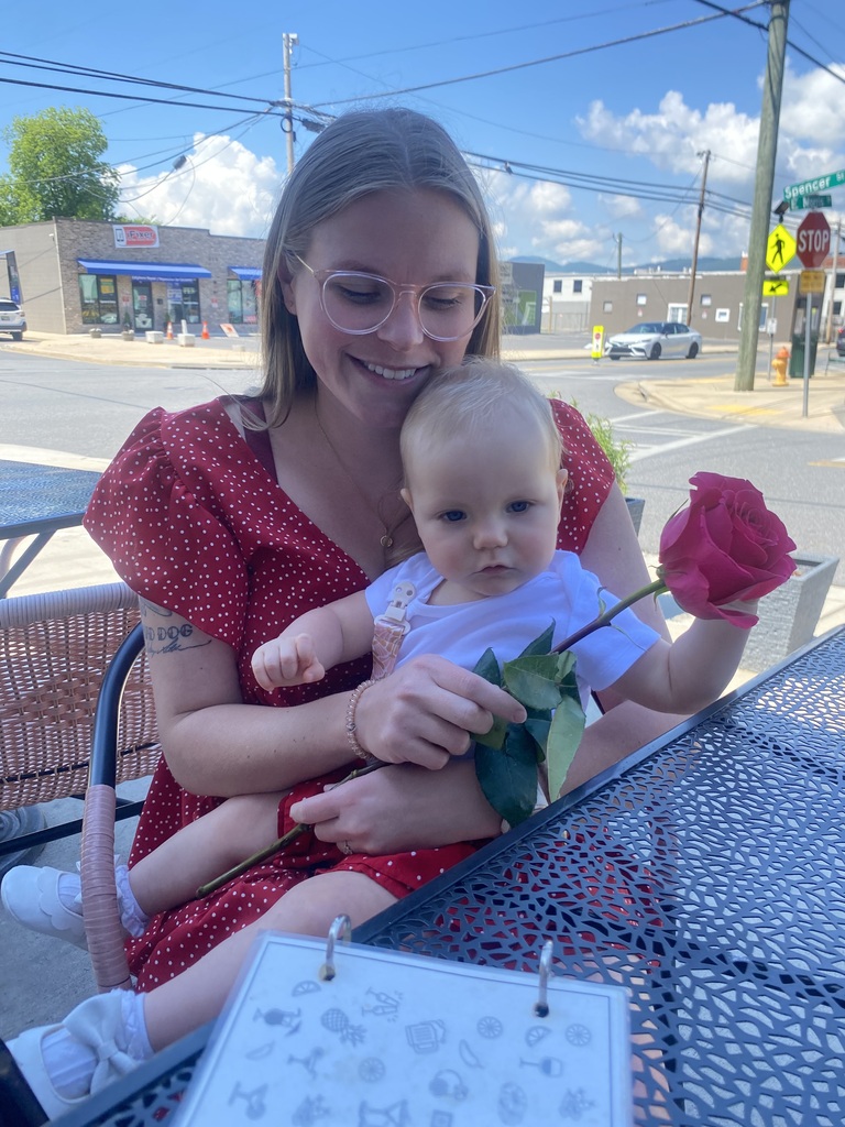 woman sits with baby on her lap. baby is holding a red rose. 