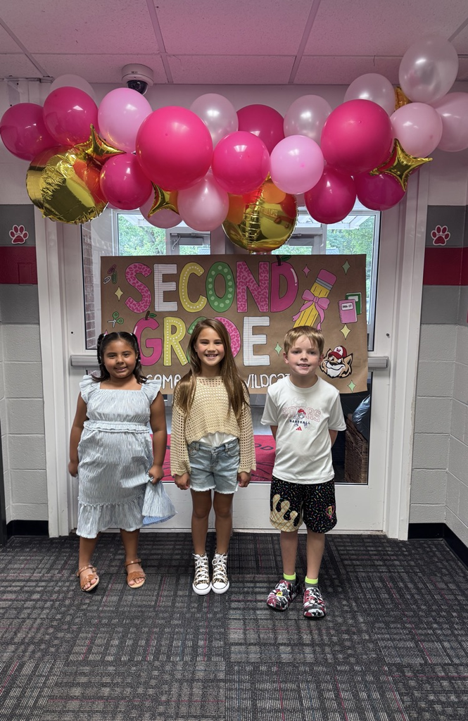 Three students standing in front of a welcome to second grade sign   
