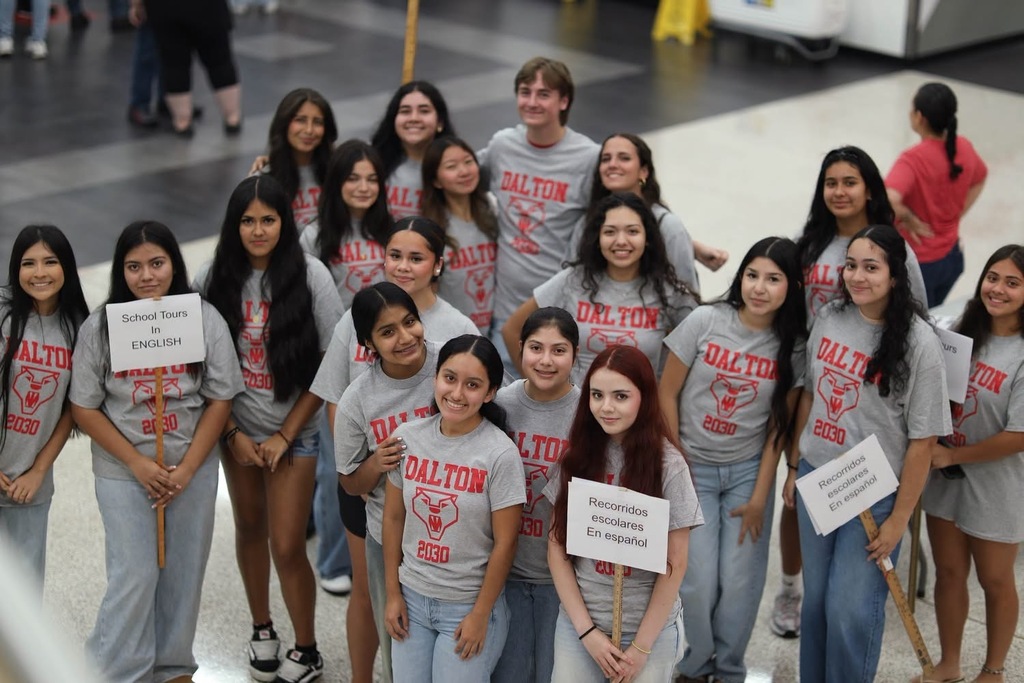A group of smiling students wearing matching grey Dalton shirts gathered and posing together indoors.