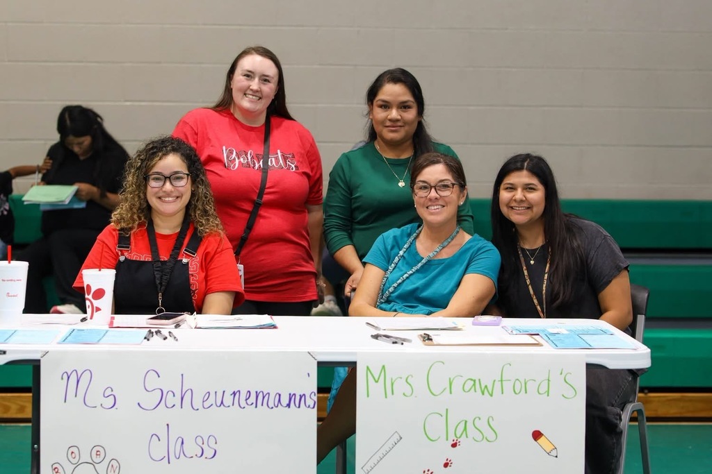 A group of five smiling school staff members posing together behind a table against a light-colored brick wall, with one woman wearing a red Dalton shirt.