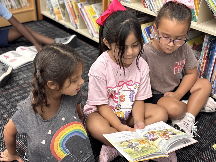 Three girls seating in the media center floor reading a book