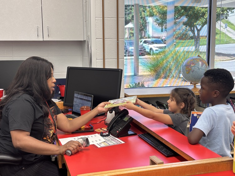 Mrs. Johnson hanging a book to a students after checking the book out