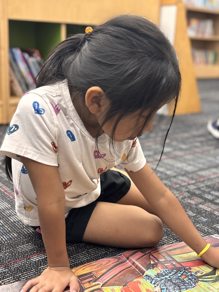 Student seating on the media center floor reading looking at picture book