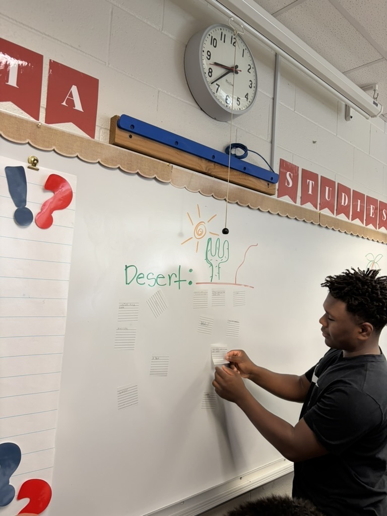 Student wearing a black shirt in a classroom writing on the whiteboard