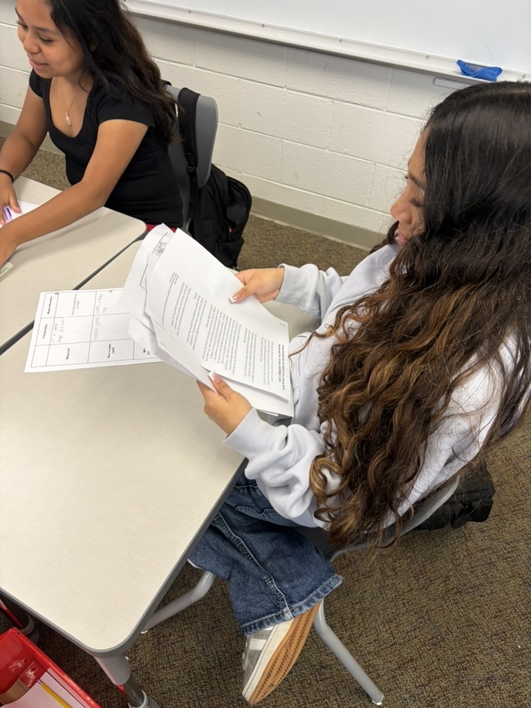 Studend sitting at a desk reading paperwork beside another student