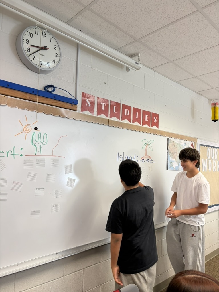 Two students in a classroom writing on the whiteboard