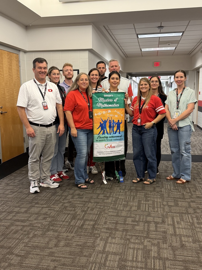 Group of educators standing in a school hallway holding a Georgia’s Masters of Mathematics banner, surrounded by four achievement ribbons recognizing student accomplishments in mathematics.
