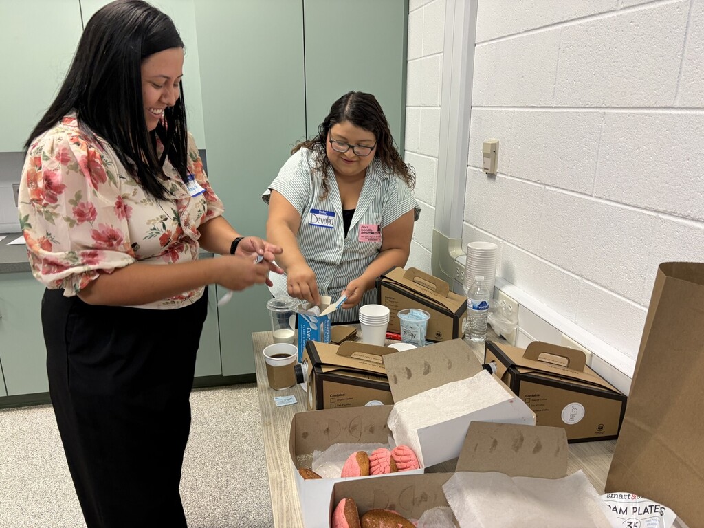 Two women setting up coffee and sweet bread for a meeting refreshment table.