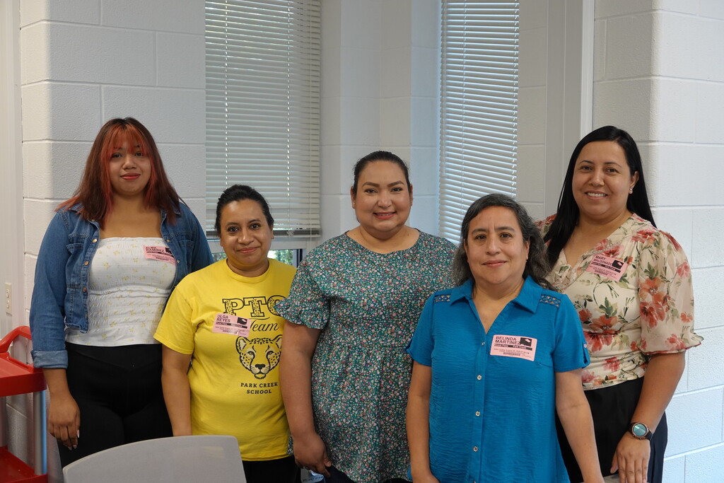 Five women standing together in a line posing for a group picture.