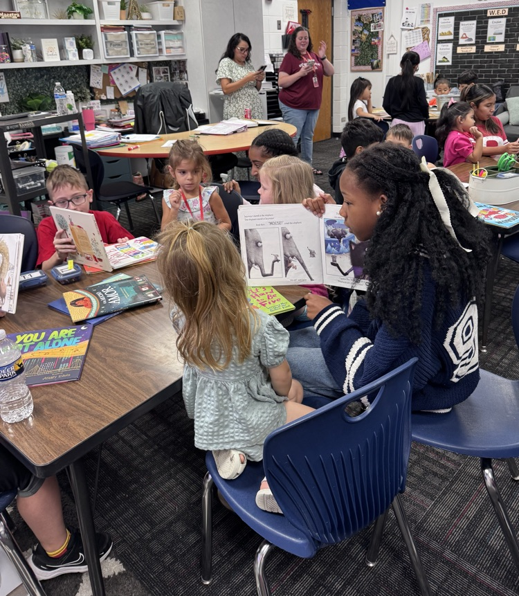 Fifth grade and PreK students sit together in a classroom reading picture books with their buddies.