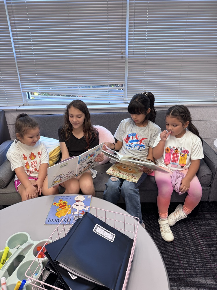 Four students sit together on a classroom couch, sharing and reading picture books during a Reading Buddies activity.