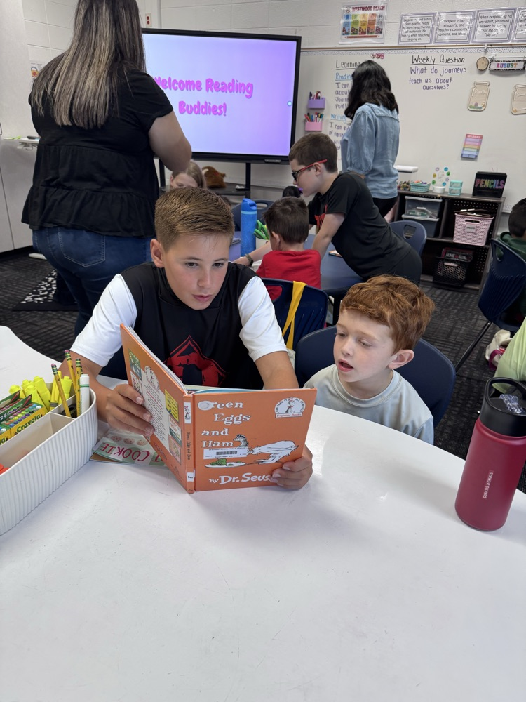 A fifth grade student reads Green Eggs and Ham with a younger reading buddy at a classroom table during Reading Buddies.