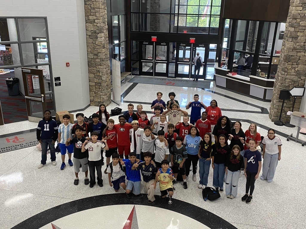 Group photo of seventh grade students celebrating Team Spirit Day at HCMS. Students are wearing jerseys and team apparel representing a variety of sports teams. The group is gathered together to show school spirit and join in the celebration of the fall sports season.