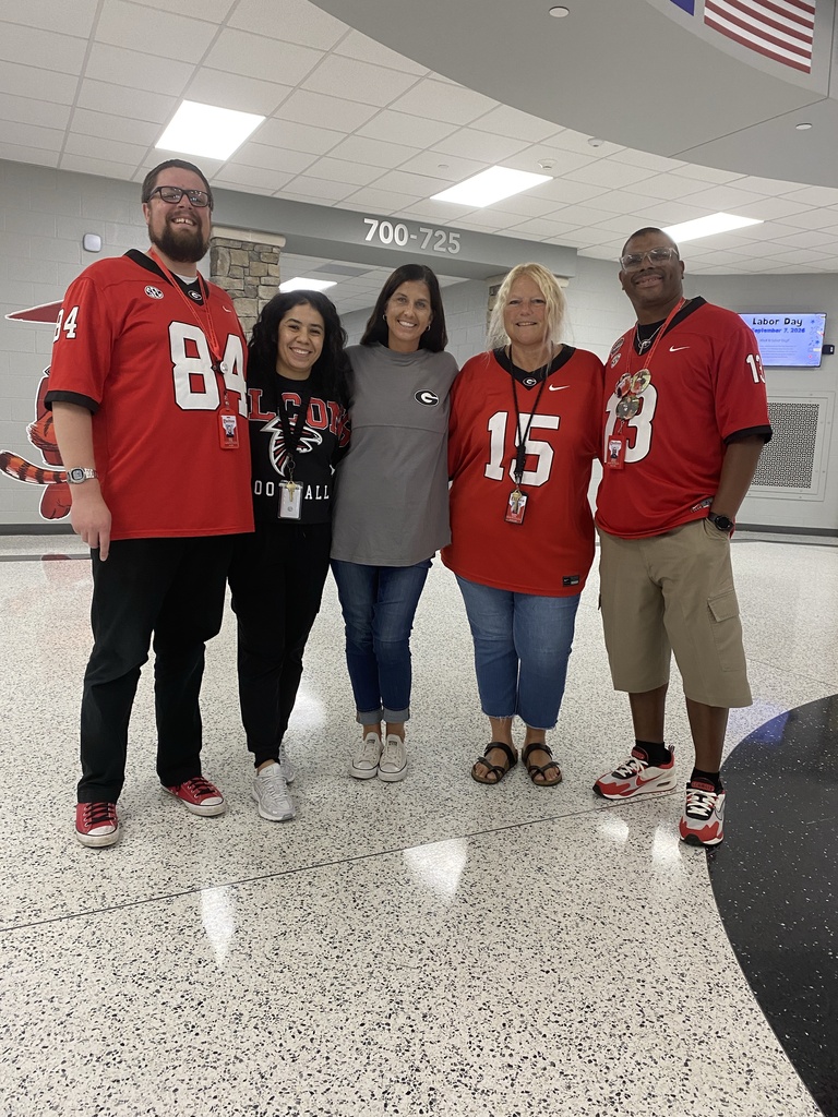 Group photo of HCMS staff members showing their team spirit in Atlanta Falcons and Georgia Bulldogs apparel. Staff members are gathered together in matching team colors for Team Spirit Day, celebrating the start of football season and sharing their favorite teams with students and colleagues.