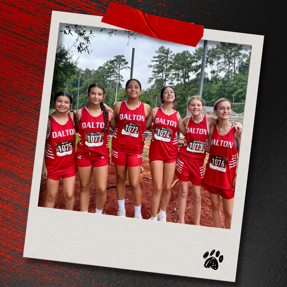 Six Dalton Middle girls cross country runners in red uniforms stand with their arms around one another and smile for a team photo. The photo is displayed in a taped Polaroid-style frame on a textured red-and-black background with a paw print accent.