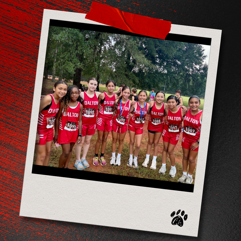 Nine Dalton Middle girls cross country runners in red uniforms pose together after the race, with two runners wearing medals. The photo is displayed in a taped Polaroid-style frame on a textured red-and-black background with a paw print accent.