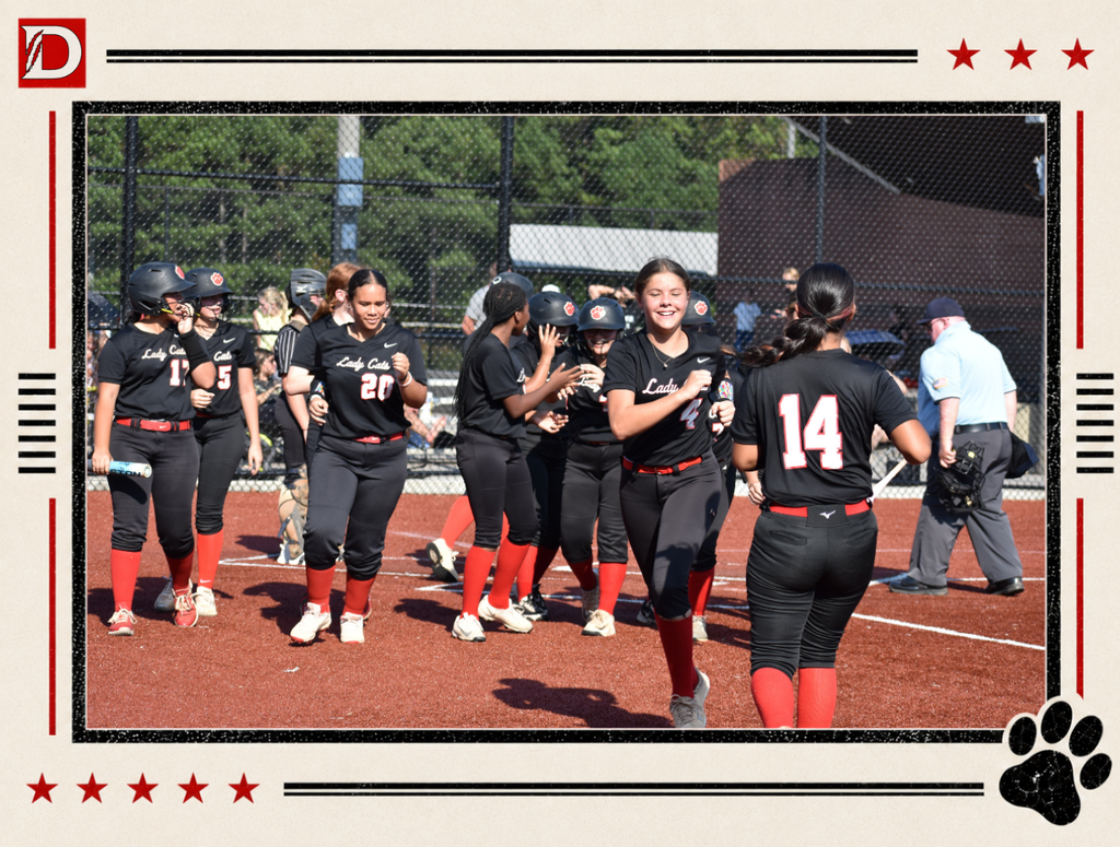 Newspaper-style Dalton Middle Athletics photo showing the Varsity Lady Cats softball team celebrating together on the field. Players in black uniforms with red socks gather near home plate, smiling and congratulating one another after a play. The photo is framed with red stars, black lines, the Dalton D logo, and a black paw print.