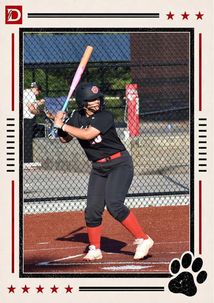 Newspaper-style Dalton Middle Athletics action photo showing a Varsity Lady Cats softball player at bat. Wearing a black uniform, red socks, and a black helmet with a red paw logo, the batter stands ready at the plate with a colorful bat raised over her shoulder. The photo is framed with red stars, black lines, the Dalton D logo, and a black paw print.