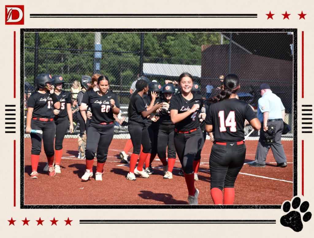 Newspaper-style Dalton Middle Athletics photo showing the Varsity Lady Cats softball team celebrating together on the field. Players in black uniforms with red socks gather near home plate, smiling and congratulating one another after a play. The photo is framed with red stars, black lines, the Dalton D logo, and a black paw print.