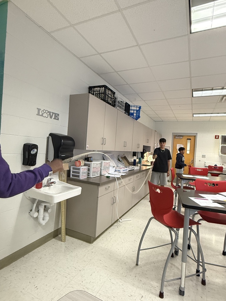 Two students in a science classroom making waves using a rope.