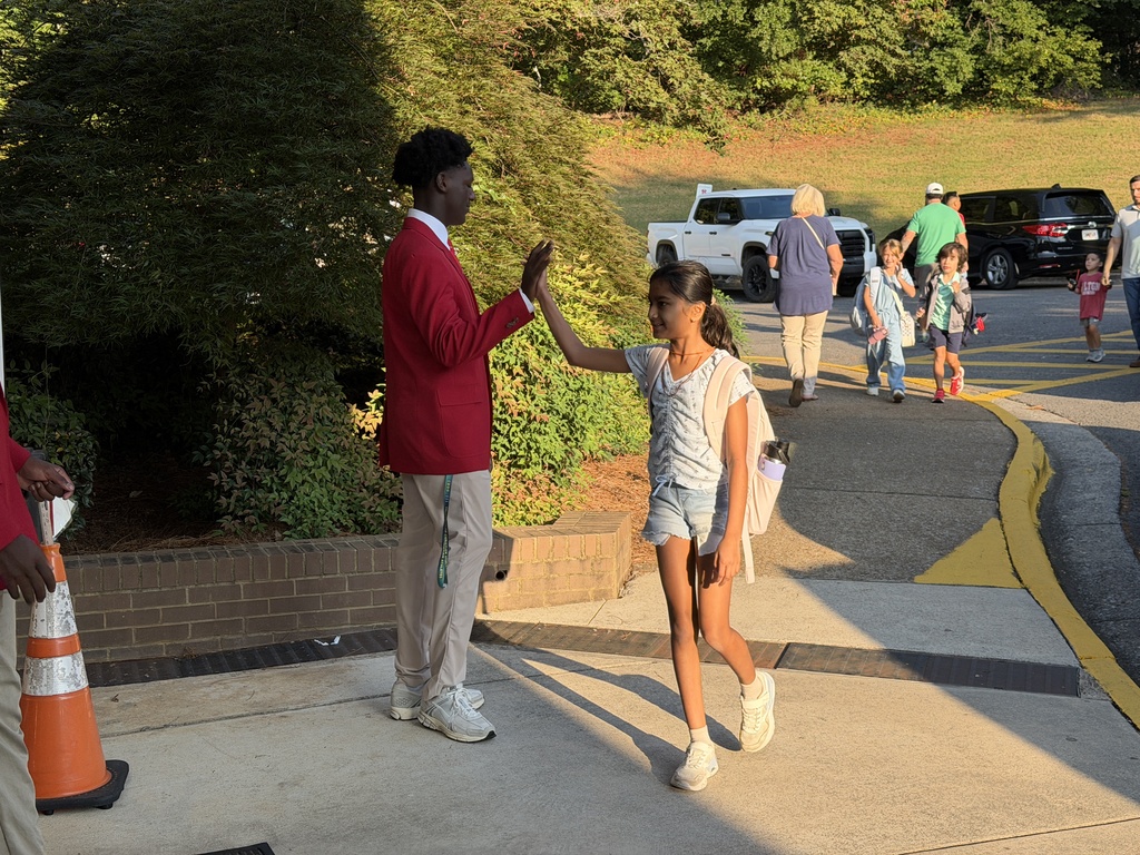 students in red jackets holding the door and high-fiving students as they enter the building