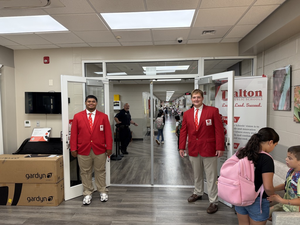 two students in red jackets holding school doors open for younger students
