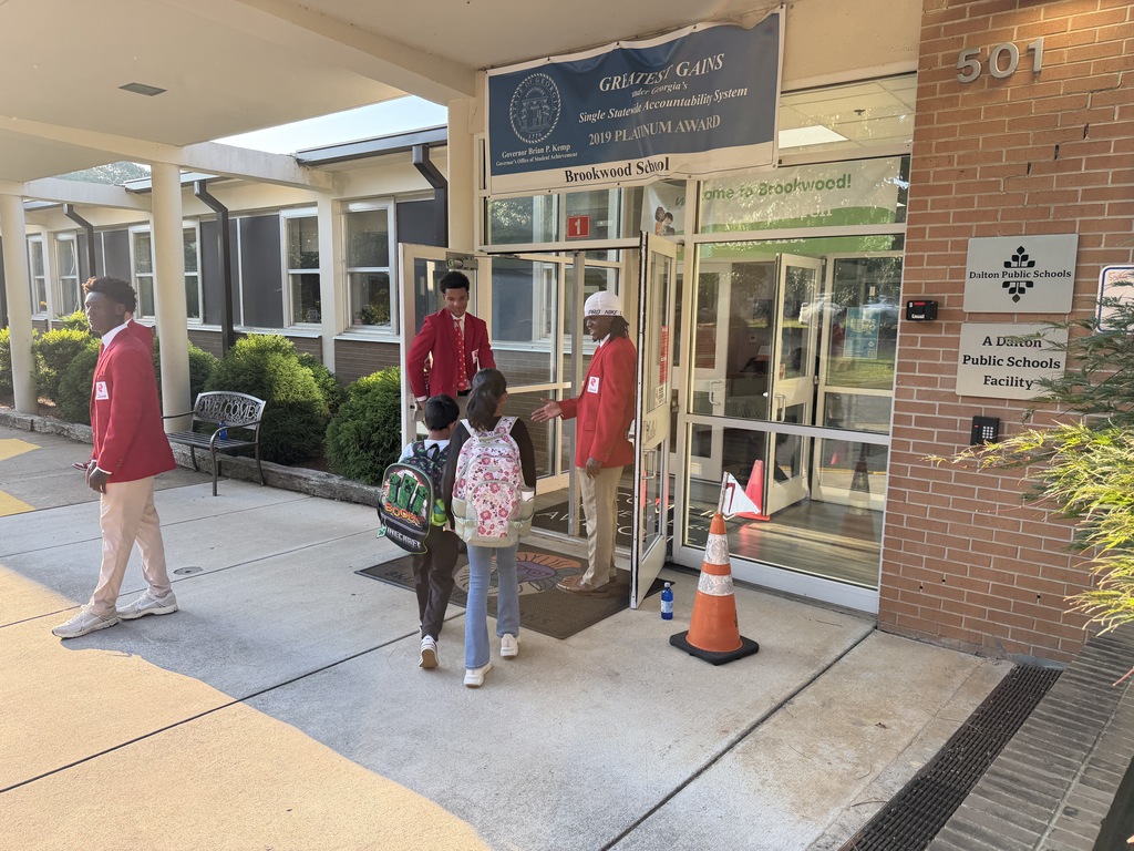 students in red jackets holding the door and high-fiving students as they enter the building