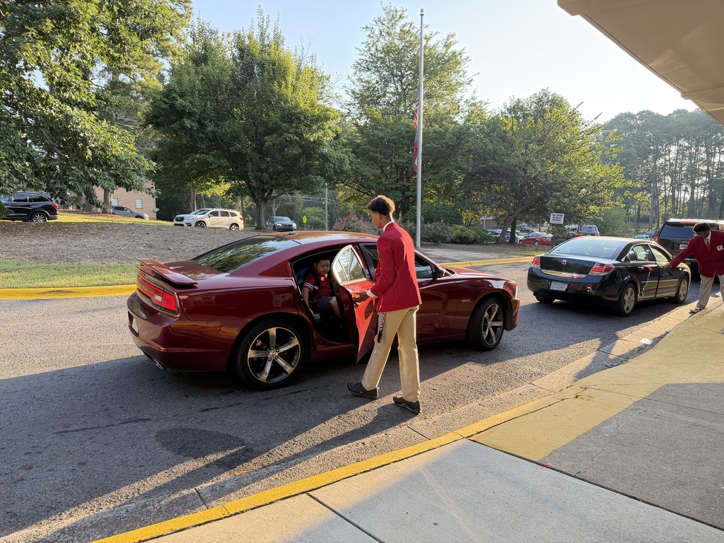 students in red jackets opening car doors for younger students