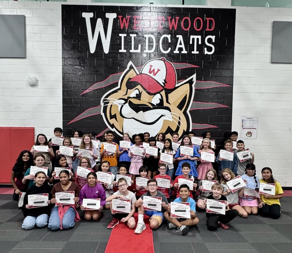 A group photo of all the student leaders sitting and standing in rows in front of a large "Westwood Wildcats" wall graphic in the school gymnasium, holding up their certificates.