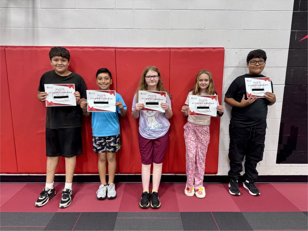 Five elementary school students posing in a row inside a gymnasium, each proudly displaying a "Student Leader" certificate.
