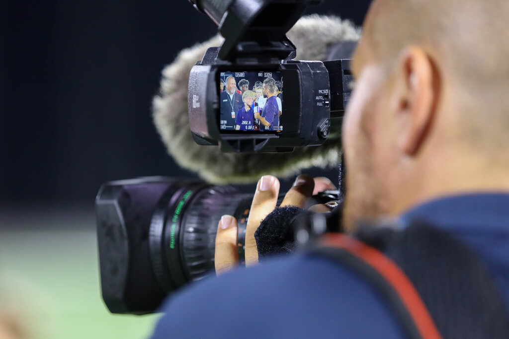 A videographer's camera screen framing an on-field student interview.