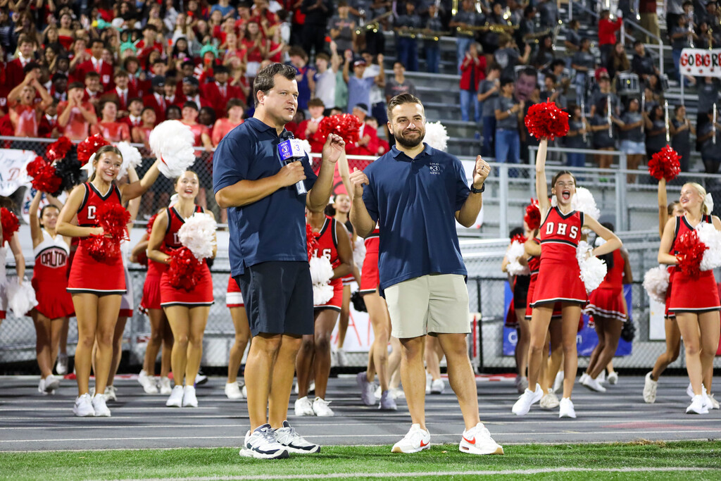 Local news reporters broadcasting live on the field flanked by Dalton High School cheerleaders.