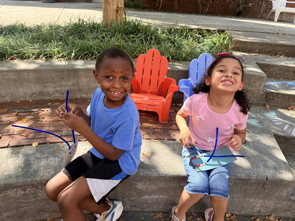 A boy in a blue shirt and a girl in a pink shirt sitting on a concrete ledge, smiling brightly a