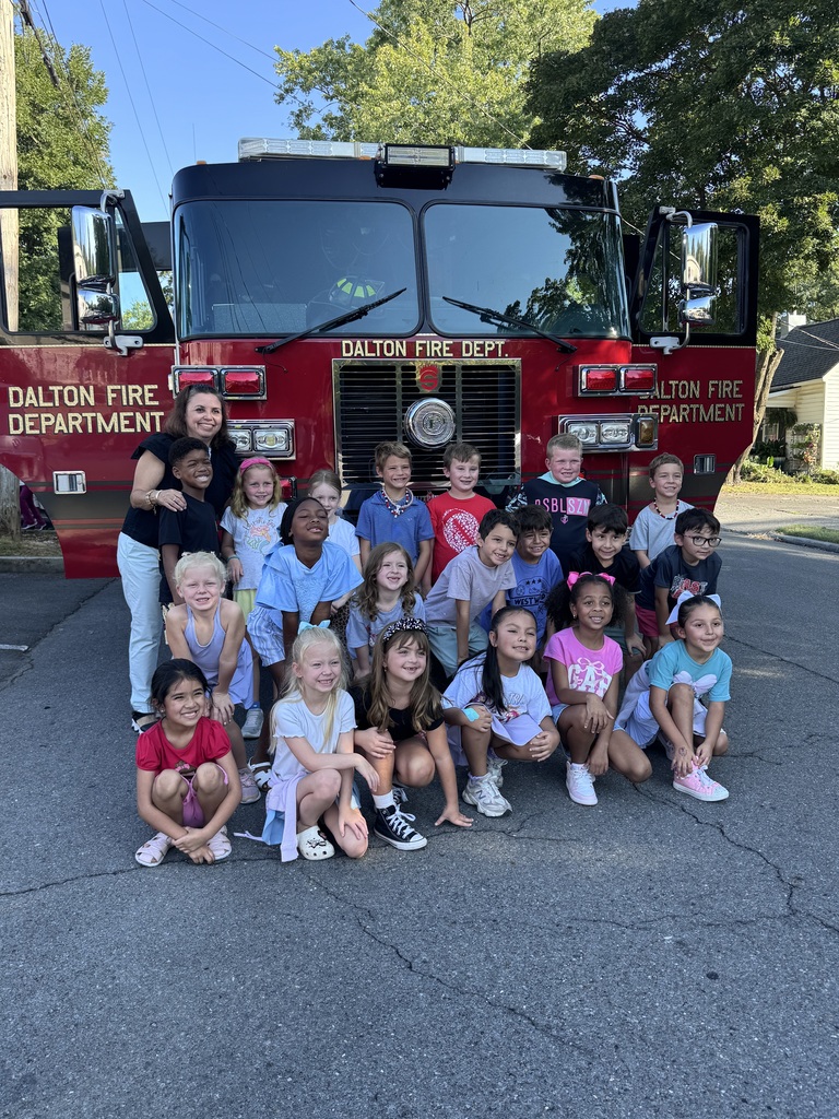 A group of elementary school students and a teacher pose for a class picture crouched and standing directly in front of a red Dalton Fire Department truck.