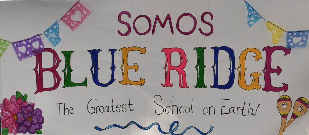 Short Alt Text (Best for web standard HTML alt attribute)  Hand-painted banner reading "SOMOS BLUE RIDGE - The Greatest School on Earth!" decorated with colorful papel picado banners, flowers, and maracas.  Long Description (Best for extended accessibility descriptions or screen reader context)  Main Text: A hand-drawn white banner with "SOMOS" in pink-outlined letters at the top, followed by "BLUE RIDGE" in large, colorful block letters, and "The Greatest School on Earth!" written in black script below.  Graphic Details:  The top of the banner features a string of colorful cut-paper banner flags (papel picado).  The bottom left corner is decorated with pink and purple flower illustrations.  The bottom right corner features two illustrated maracas decorated with paw prints.