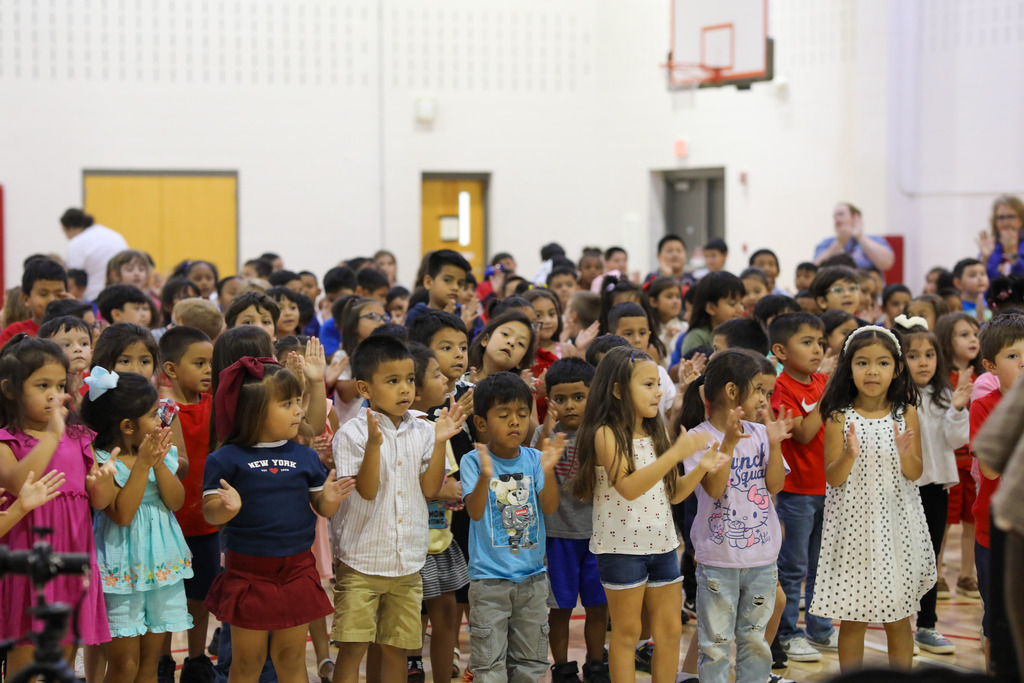 A large group of elementary students sitting together and clapping during a gym presentation.