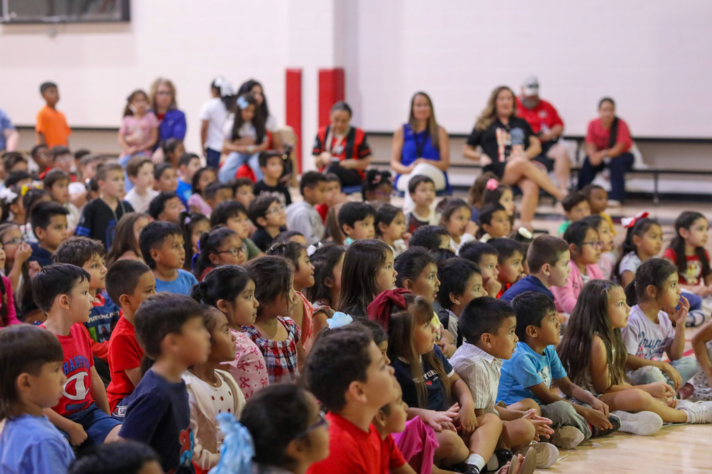 Elementary students sitting on the gymnasium floor listening to an interactive educational show.