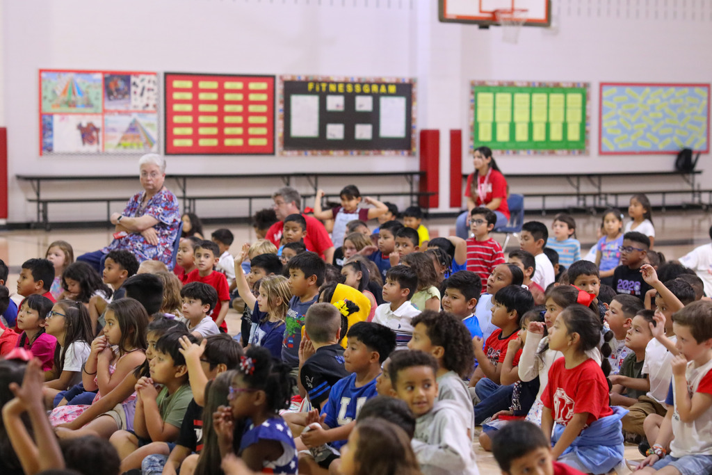 Elementary students clapping along with a costumed presenter during a school assembly.