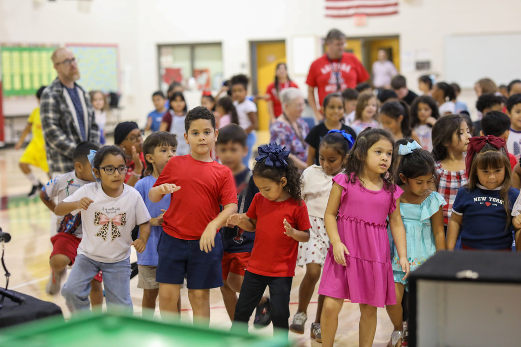 Elementary students standing and dancing along during an interactive school assembly in a gymnasium.