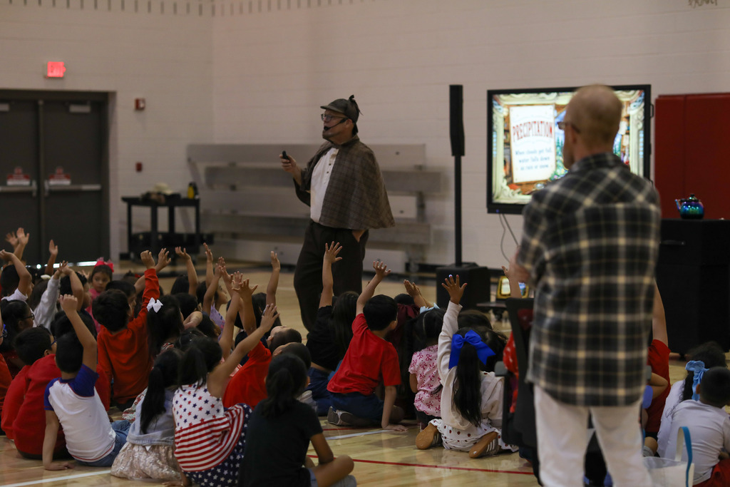 Students raising their hands to answer questions during a science presentation about precipitation.