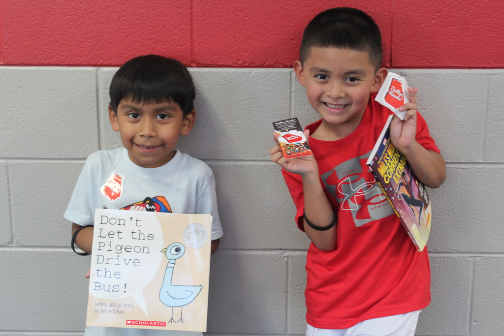 Two young boys smiling and holding up their new books and Dalton Reads stickers in front of a gray brick wall.