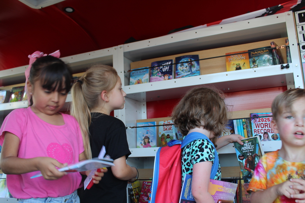 Four young students browsing shelves of children's books inside the Dalton Reads Van.