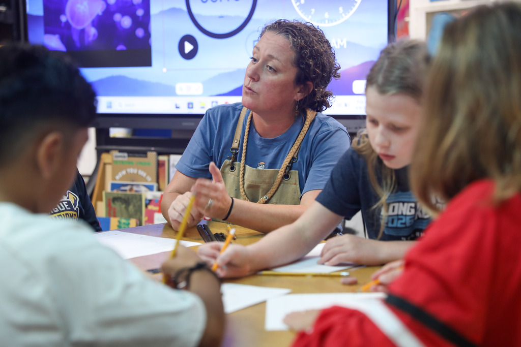 An art teacher seated with elementary students guiding them through a drawing project.