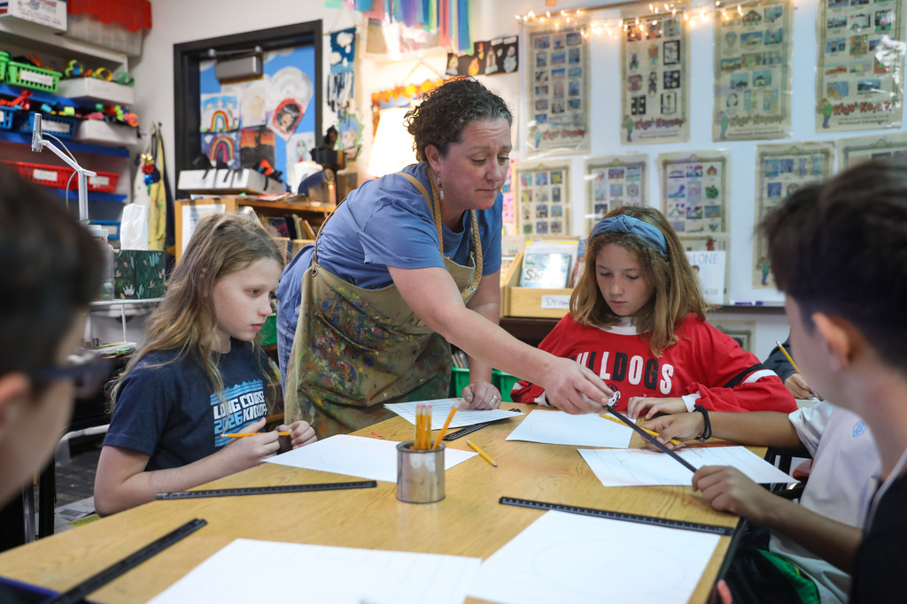 An art teacher leaning over a student's desk to demonstrate line drawing techniques.