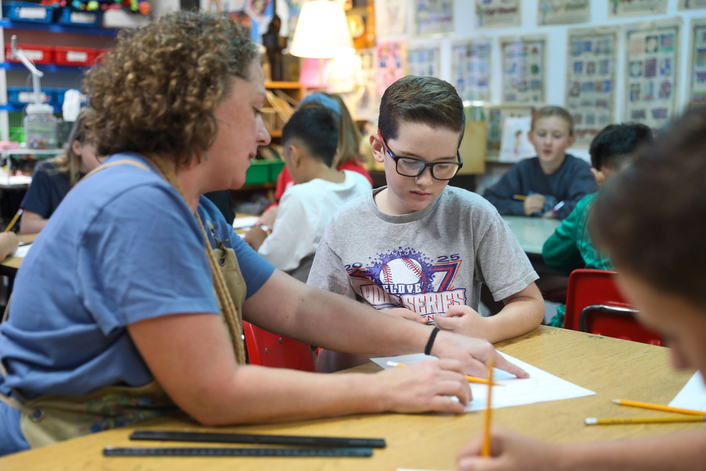 An art teacher pointing out details on a student's drawing at a work table.